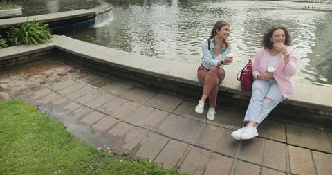 Two women chatting by fountain with coffee cups casual outdoor friendship moment