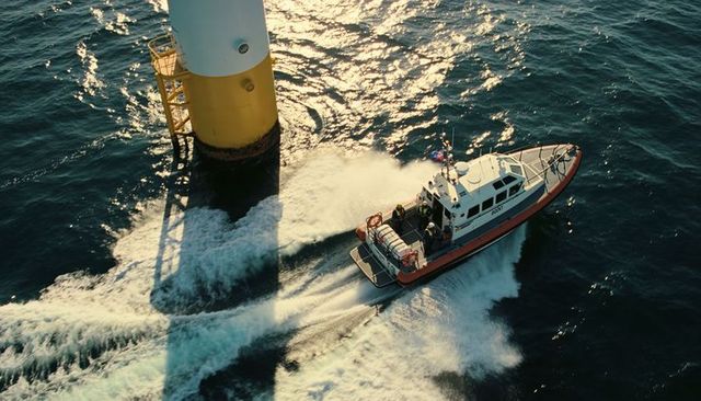 Orange rescue boat racing past offshore wind tower creating dramatic wake and spray sunset