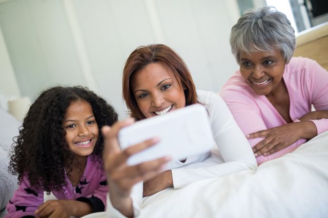 Multigenerational family enjoying quality time together, capturing a happy moment with a selfie in a cozy bedroom. Ideal for use in advertisements promoting family bonding, technology use in everyday life, or home lifestyle content.