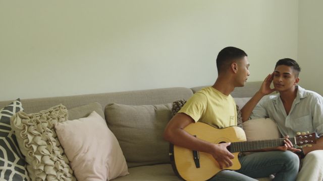 Gay couple enjoying quality time at home, one playing guitar while the other listens, perfect for illustrations on love, relationships, or LGBTQ+ themes. Emphasizes connections and romance in a cozy home environment.