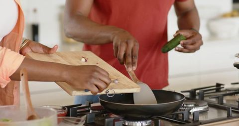 African american couple cooking together pouring garlic into skillet on gas stove