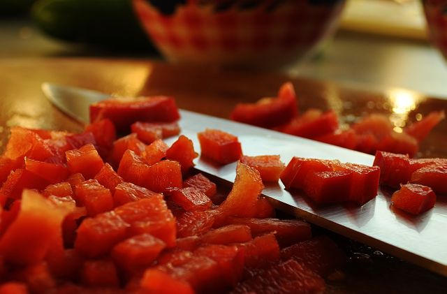 Close-up of freshly chopped red bell peppers on a wooden cutting board with a sharp kitchen knife. Ideal for content on cooking, recipes, healthy eating, food blogs, culinary tutorials, and kitchen tools.