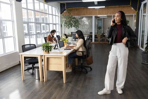 Professional woman talking on phone in bright modern coworking space with colleagues