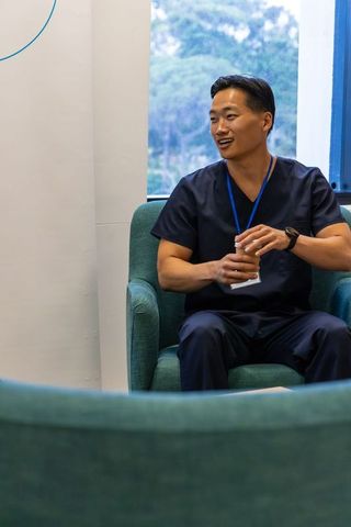 Asian man smiling and chatting in staff lounge wearing navy scrubs and lanyard