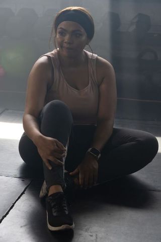 African american woman sitting on gym floor holding ankle post-workout moody rim light