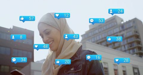 Smiling woman wearing beige hijab checking smartphone with social media notifications