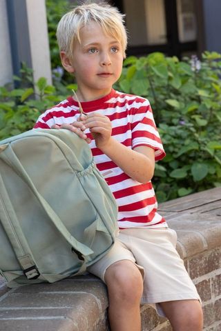 School-age boy sitting on brick ledge with backpack, gazing thoughtfully in courtyard