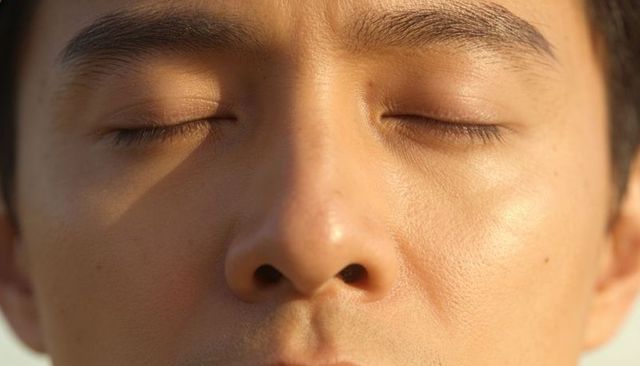 Golden hour closeup headshot of sunlit asian male face showing skin texture and pores