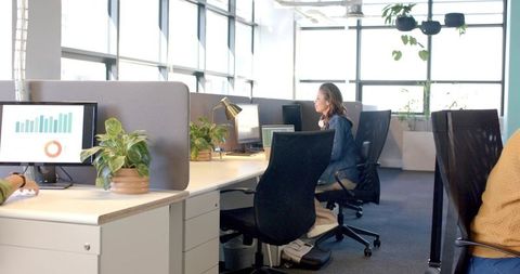 Young professional working at modern open-plan office desk with ergonomic chair and plants