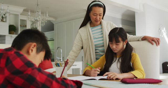 Asian mother in kitchen helping son and daughter doing schoolwork - Download Free Stock Photos Pikwizard.com