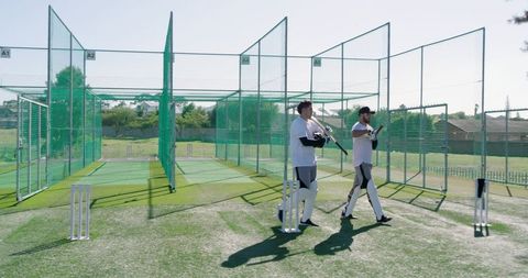 Cricket teammates walking to outdoor net practice carrying bats and wearing pads