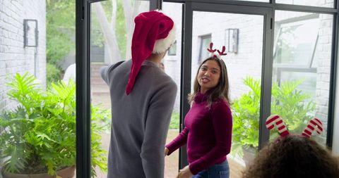Family welcoming guests wearing santa hat and reindeer headbands by glass patio doors