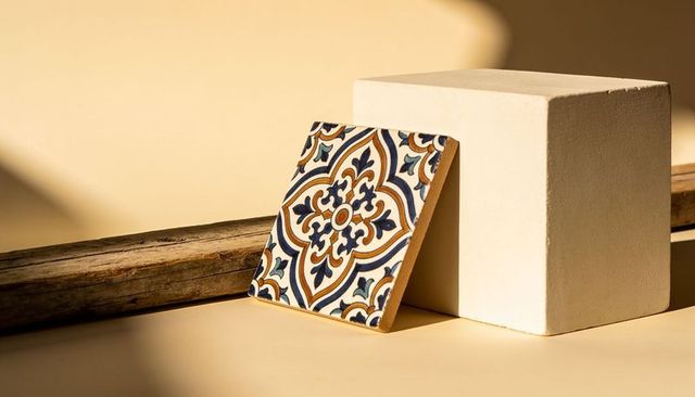 Leaning ornate ceramic tile against geometric white block on warm beige tabletop