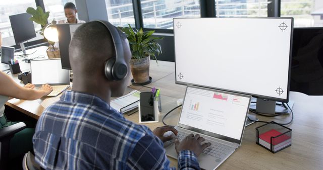 African american businessman using computer with blank screen in office, copy space. Casual business, office, work, professionals concept, unaltered.