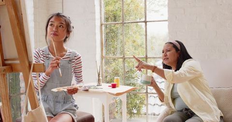 Young artist painting on easel guided by instructor in cozy studio