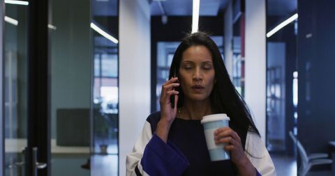 Businesswoman Holding Coffee Talking on Smartphone in Office