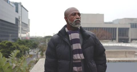 Senior african american man standing on urban rooftop in puffer jacket and striped scarf