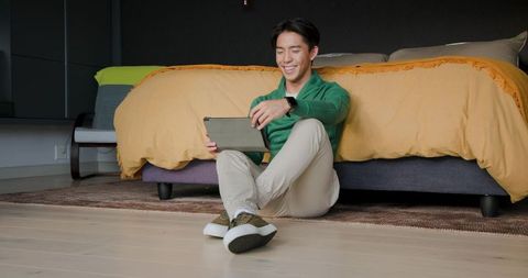 Modern Asian Man Relaxing in Bedroom with Tablet and Smartwatch