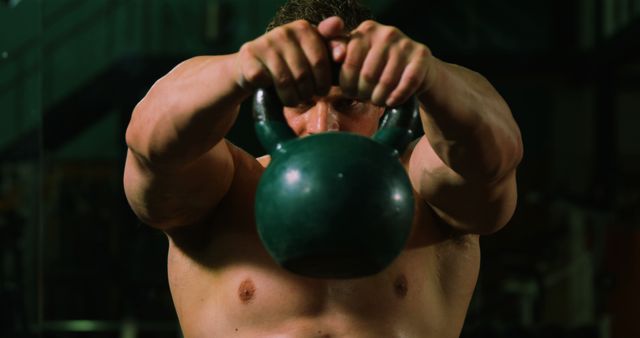 Man displays strength and fitness while lifting a kettlebell in a gym. Perfect for promoting fitness programs, workout routines, strength training tips, bodybuilding websites, and health-related publications.