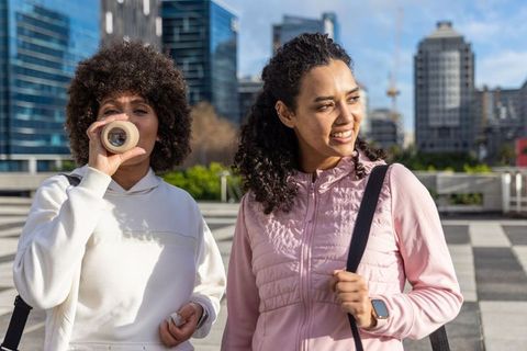 Two women walking in urban plaza drinking from reusable bottle smiling with smartwatch