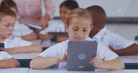 Elementary girl using tablet while classmates learning on devices in classroom