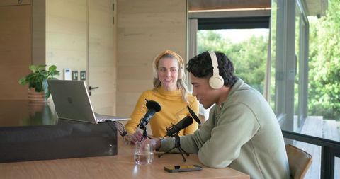 Young diverse co-hosts recording podcast in bright modern home studio with microphones