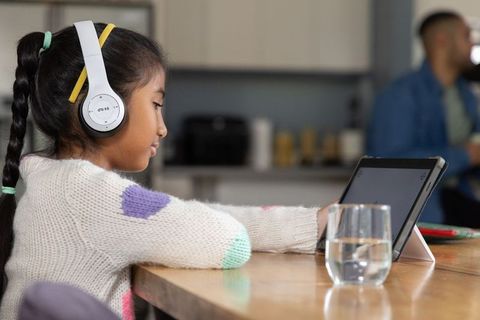Child wearing headphones using tablet at kitchen table parent nearby cozy home learning