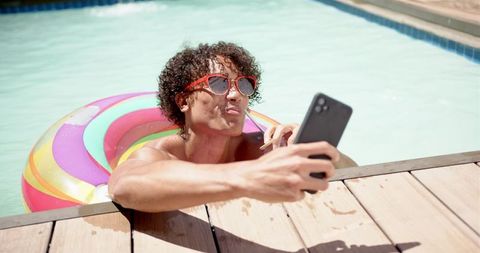 Man Lounges In Inflatable Pool Using Smartphone On A Sunny Day