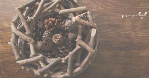 Woven twig basket with pine cones on rustic wood table with handwritten math overlay