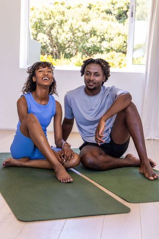 Sunlit african american couple sitting on yoga mats holding hands after workout