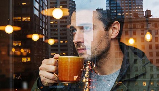 Contemplative man holding ceramic mug gazing through cafe window with city reflections