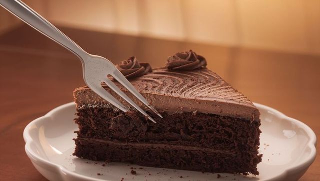 Fork slicing decadent layered chocolate cake with smooth ganache frosting and rosette piping