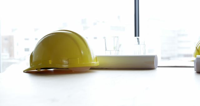 Yellow hard hat and rolled building plans on a design table at construction site. This stock photo can be used for promotional materials, safety training manuals, construction company websites, or engineering presentations.