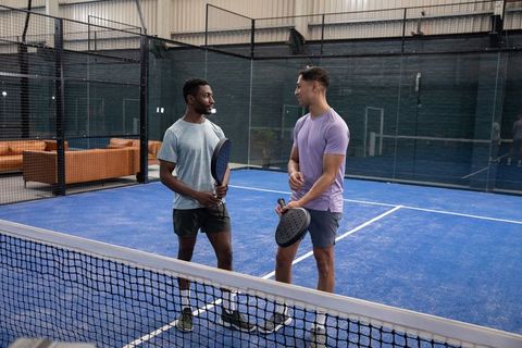 Men chatting and holding padel rackets on indoor blue court during training session