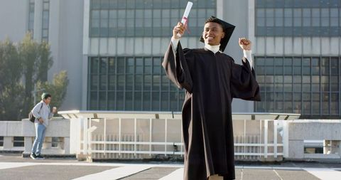 Jubilant african american graduate raising diploma and celebrating on campus plaza