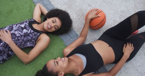 Happy twin sisters relaxing with basketball in park