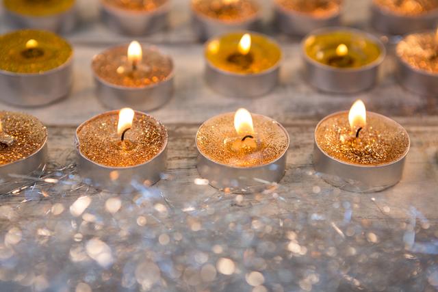 This image of glittering tealight candles burning on a wooden surface is perfect for holiday-themed projects, Christmas cards, festive event invitations, or home decor inspiration. The warm glow and sparkling details create a cozy and celebratory ambiance, ideal for promoting seasonal products or creating a festive mood in marketing materials.