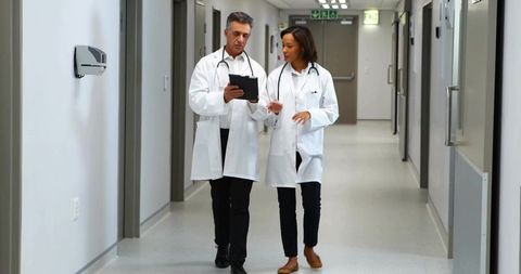 Two Doctors Discussing Patient Notes While Walking in Hospital