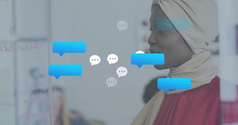 Hijab-clad businesswoman collaborating at glass board with blue chat bubble overlays