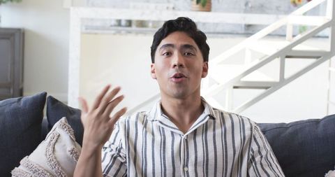 Young Asian man speaking and gesturing on sofa in modern minimalist living room interior