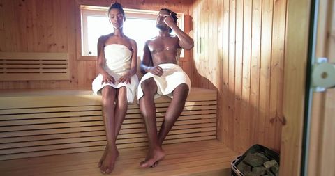 African american couple relaxing in wooden sauna wearing towels, steam and intimacy