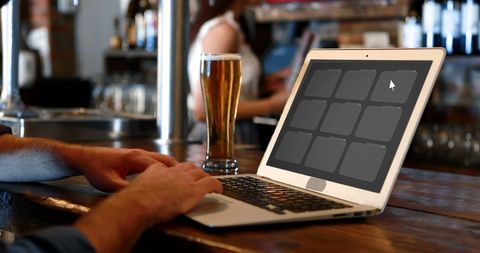Working on laptop in casual bar setting with beer