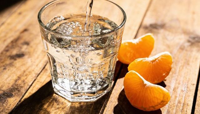 Pouring water into faceted glass beside tangerine segments on sunlit wooden table