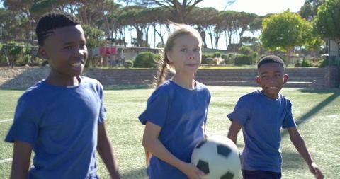 Diverse youth playing soccer on sunny turf holding ball smiling teamwork and friendship