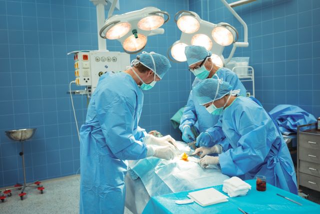 Medical professionals are performing a surgical procedure in a sterile hospital operating room. Surgeons are focused and coordinated, showcasing teamwork and precision. This image can be used to illustrate topics related to healthcare, medical services, surgical teams, hospital care, and professional medical environments.