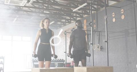 Man and woman performing dumbbell step-ups at industrial crossfit gym partner workout