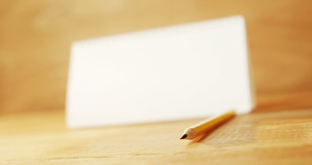 A blank white card rests on a wooden surface next to a pencil, with copy space. Ideal for a personalized message or name placement, the setup suggests preparation for an event or identification.