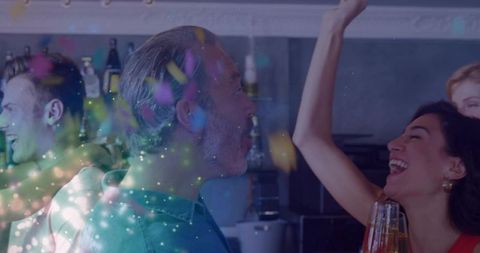 Friends toasting in home kitchen with confetti and cocktails celebrating together