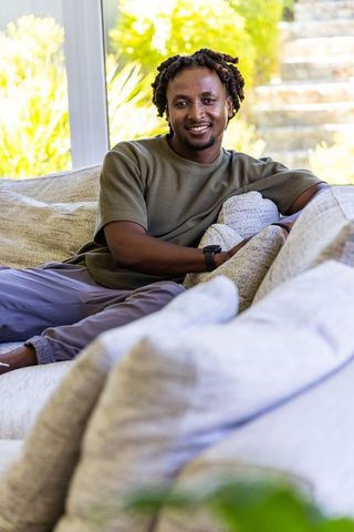 African american man relaxing on bright sofa, smiling in sunlit modern living room