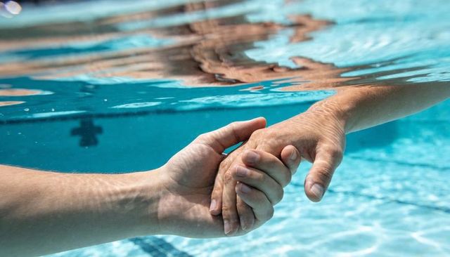 Underwater close-up of hands holding and supporting partner in pool conveying trust and care